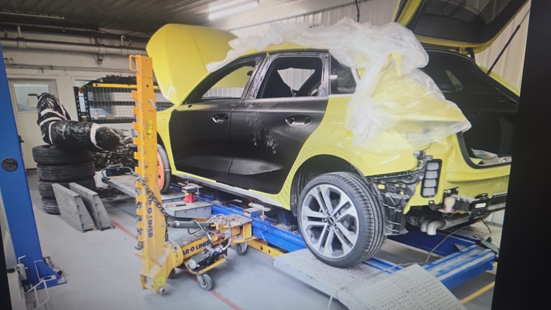Yellow Audi A3 undergoing body repairs on workshop alignment equipment